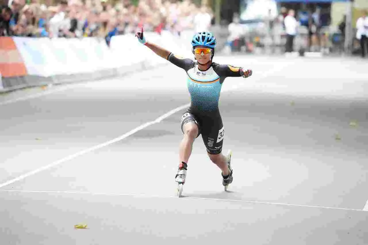 Inline skater viert direct na de finish een sportmoment met een arm omhoog.